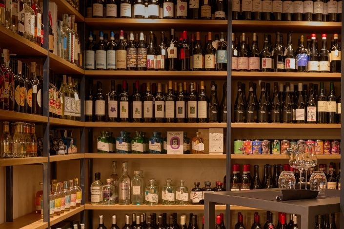 Scaffali di legno di un'enoteca ben fornita con numerose bottiglie di vino, liquori e distillati di vario tipo.