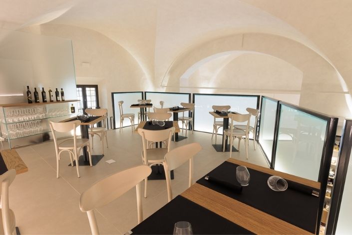 Interno luminoso e moderno dell'enoteca Emporio San Lorenzo a Ferrara con tavoli apparecchiati e scaffali di vini.