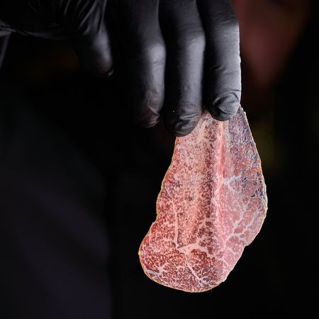 Mano guantata che tiene una sottile fetta di bresaola di Wagyu con intensa marezzatura