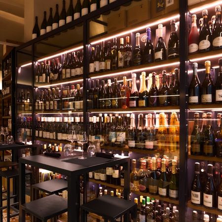 Interno elegante dell'enoteca Emporio San Lorenzo con scaffali illuminati pieni di bottiglie di vino di diverse etichette e tavolini con calici pronti.