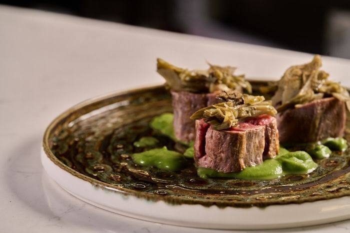 Tre medaglioni di carne al sangue guarniti con verdure in un piatto decorato