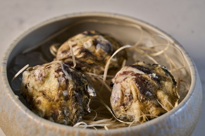 Tre ostriche fresche presentate in una ciotola di ceramica su un letto di paglia.